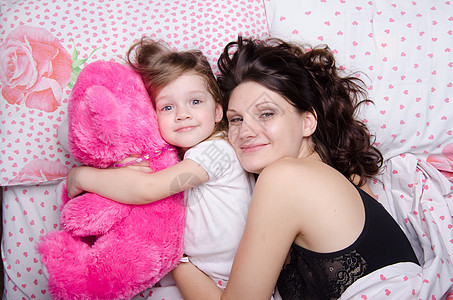 妈妈抱着她女儿躺在床上孩子们拥抱乐趣童年寝具父母幸福枕头家庭教育图片