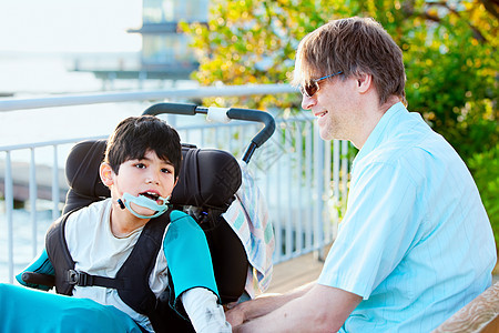 父亲在户外轮椅上与残疾儿子交谈图片