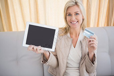 漂亮的金发美女在线购物 用平板电脑微笑住所房子长椅电子商务女性触摸屏休闲家庭信用卡图片