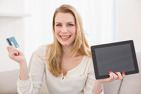 漂亮的金发美女在线购物 用平板电脑住所服装微笑沙发公寓药片互联网长椅信用卡客厅图片