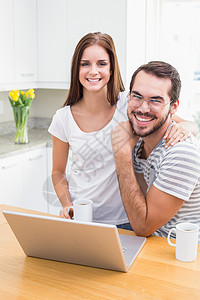 年轻夫妇用笔记本电脑对相机微笑图片