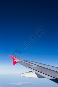 机翼飞机在云上飞翔 从西向天空仰望蓝色窗户运输引擎翅膀技术喷射红色白色旅行图片