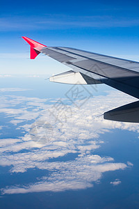 机翼飞机在云上飞翔 从西向天空仰望喷射旅行白色翅膀运输红色窗户航班技术蓝色图片