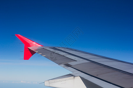 机翼飞机在云上飞翔 从西向天空仰望红色引擎蓝色窗户喷射技术旅行运输翅膀白色图片