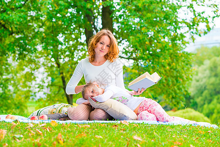 美丽的母亲和女儿在公园里休息 阅读一本书图片