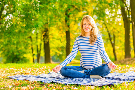 在公园里快乐的孕妇 坐在莲花阳地上图片