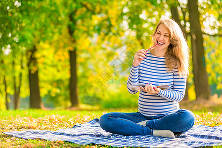 在公园里拿着笔记本的年轻快乐怀孕少女图片