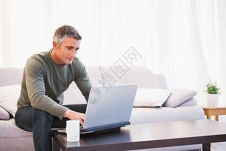 坐在沙发上用笔记本电脑的人技术家庭生活杯子男人男性公寓微笑房子服装休闲图片