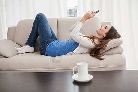漂亮的黑发美女在沙发上发短信客厅技术长椅电话住所家庭生活手机热饮闲暇棕色图片