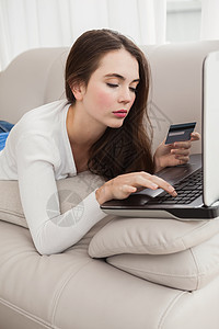 漂亮的黑发美女在沙发上网上购物网站闲暇男性家庭头发笔记本长椅技术房子说谎图片