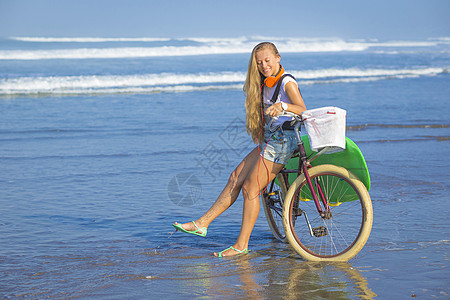 带冲浪板和自行车的年轻女孩微笑海滩热带比基尼青少年木板海洋冲浪海浪金发图片