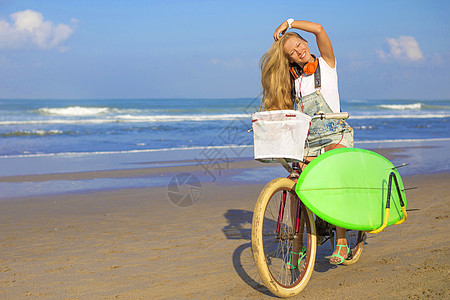 带冲浪板和自行车的年轻女孩运动木板海滩金发海洋热带海浪冲浪青少年金发女郎图片