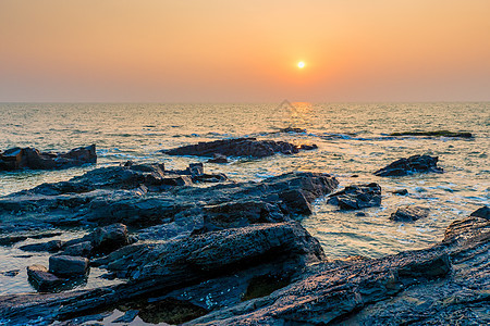 海面和岩石海岸的明橙色太阳图片