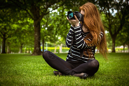 坐在草地上的女摄影师单反相机技术摄影绿地女性闲暇长发爱好公园背景图片