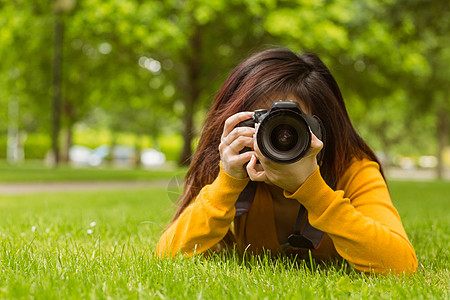 公园女摄影师草地棕色说谎女性单反绿地相机摄影技术头发背景图片