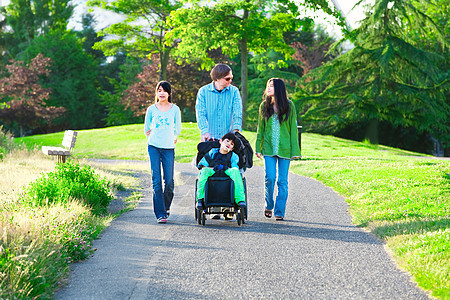 坐在轮椅上的残疾男孩与家人一起在阳光下户外散步图片