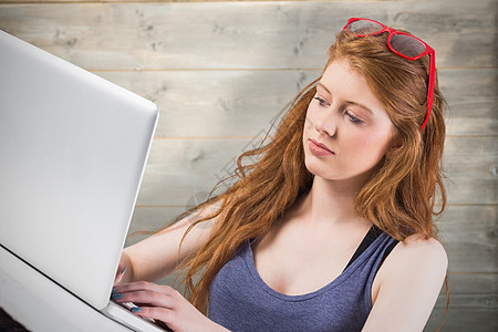 在笔记本电脑上工作的漂亮红头发的复合图像红发木板学生木头绘图眼镜女性背心潮人学习图片