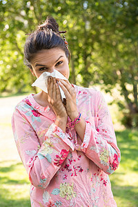 漂亮的黑发美女吹她的鼻子阳光休闲公园碎花感染流感疾病女士花粉组织图片