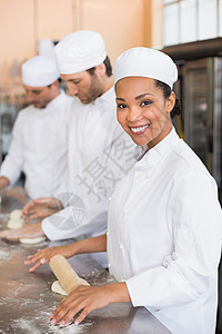 面包师小组在柜台工作团队混血制服男性微笑面包面团职业厨房擀面杖图片