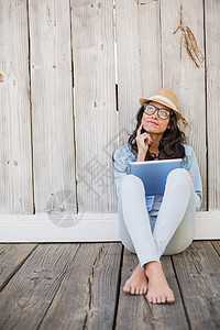 坐在地上用平板电脑坐着时髦的嬉皮士赤脚外套草帽微笑思维牛仔闲暇木头女性毡帽图片