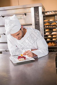 专心面包师在糕点上放鲜花和水果食物甜点职员厨师制服职业蛋糕厨房男性商业图片