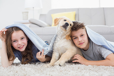 在客厅内用毯子下带狗的可爱兄弟姐妹图片