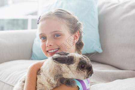 快乐的女孩把兔子放在起居室客厅宠物家畜童年家庭生活沙发休息室房子女性闲暇图片