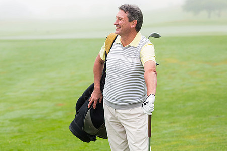 英俊的高尔夫球手拿着高尔夫袋站立假期高尔夫手套微笑运动员闲暇时间黑色绿色享受背景图片