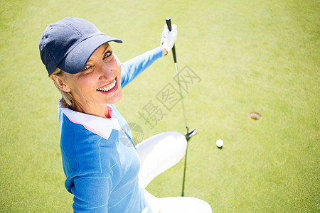 微笑的女士高尔夫球手跪在绿色上休闲高尔夫女性爱好运动员晴天时间毛衣运动背心图片