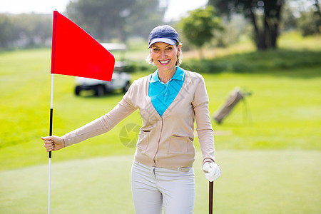 女性高尔夫球手在相机上微笑并抱着她的高尔夫俱乐部图片