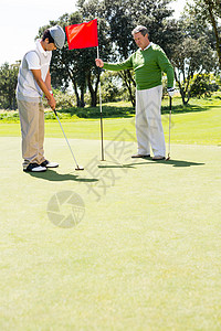 Golfer 为朋友投球持洞旗晴天闲暇高尔夫运动员手套旗帜男性运动活动专注图片