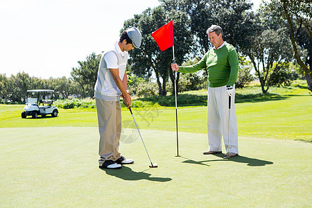 Golfer 为朋友投球持洞旗爱好旗杆旗帜运动假期阳光老年高尔夫球闲暇友谊图片