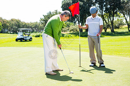 Golfer 为朋友投球持洞旗老年友谊手套活动旗帜绿色运动员假期专注高尔夫球图片