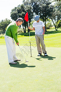 Golfer 为朋友投球持洞旗活动旗杆专注老年高尔夫球阳光推杆男性假期运动员图片