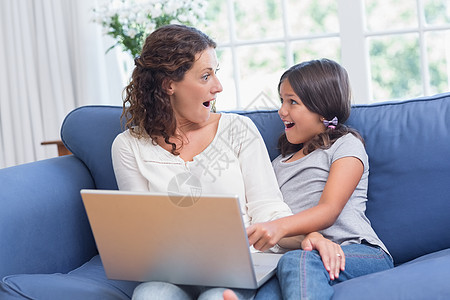 快乐的母亲和女儿坐在沙发上 使用笔记本电脑房子女孩长椅微笑震惊家庭生活服装客厅女性卷发图片