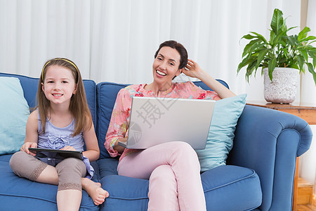 母亲和女儿使用平板电脑和笔记本电脑公寓快乐沙发服装长椅客厅家庭触摸屏住所女性图片