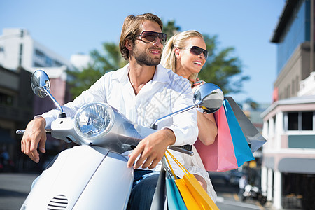迷人的情侣骑摩托车零售助力车微笑骑术活动感情交通潮人快乐购物袋背景图片