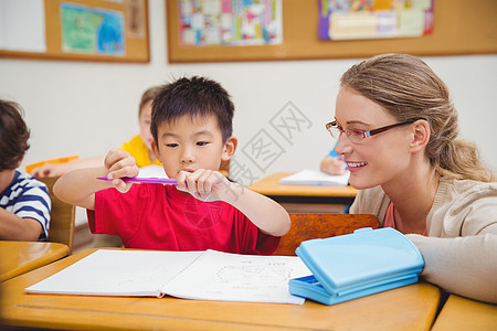 美貌教师帮助教室中的学生笔记本同学们职业童年女士桌子小学生椅子瞳孔知识图片