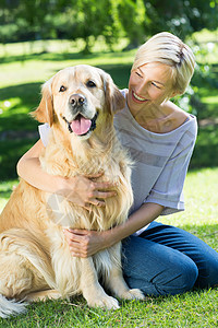 金毛猎犬在公园拥抱她的狗的金发快乐微笑家畜晴天闲暇宠物阳光女性农村金发女郎草地背景