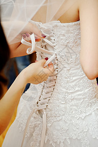 伴娘在帮新娘穿衣服蕾丝婚礼胸衣设计师身体成人庆典纺织品婚姻丝带图片