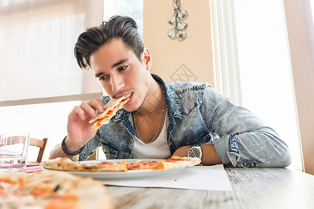 英俊的年轻人在家里吃披萨图片
