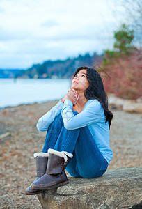 少女坐在湖岸边的巨石上祈祷图片