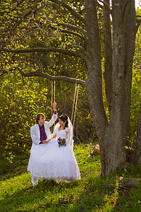 新娘和新郎在秋千上摇摆野花夫妻女性拥抱花束裙子草地天空婚礼公园图片