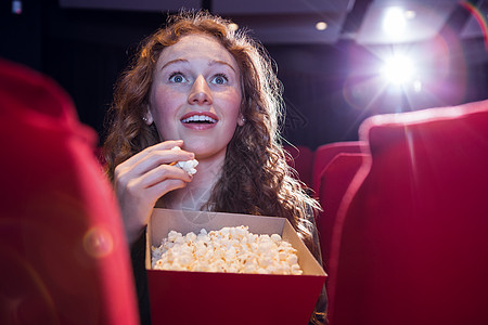 文艺演出微笑的年轻女子在看电影座位文艺闲暇红色时间快乐爆米花电影娱乐电影院背景