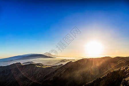 太阳在蓝天的山上照耀天空火山阴霾日落阳光蓝色图片