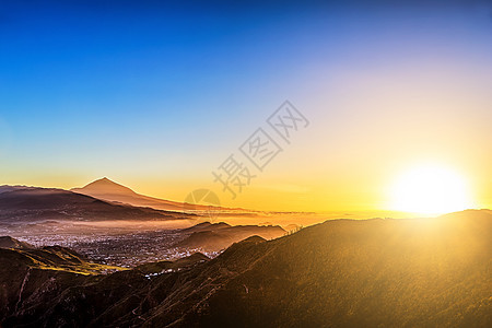 太阳在蓝天的山上照耀阴霾阳光天空日落背景蓝色火山图片