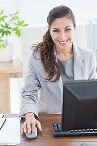微笑的女商务人士看着相机电脑屏幕人士女性长发电子套装公司商务桌子图片
