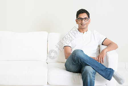 坐在沙发上的英俊帅气的印度年轻人学生男人商业白色眼镜房子男性公寓大学微笑图片