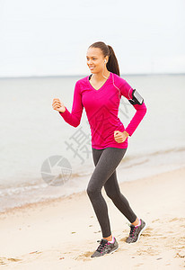 微笑着的女士在户外田径上奔跑列表手机细胞播客运动服跑步赛跑者重量音乐海滩图片