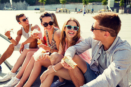 一群笑着的朋友坐在市广场上男人太阳镜乐趣假期女性友谊垃圾游客会议热狗图片